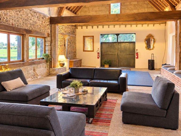 Canapés et table basse dans la grande salle de la grange, murs de silex et grande porte