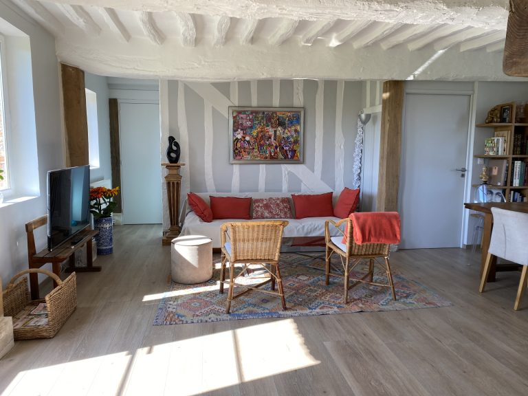 Salon aux colombages et canapé rouge, pièce de vie commune de la longère